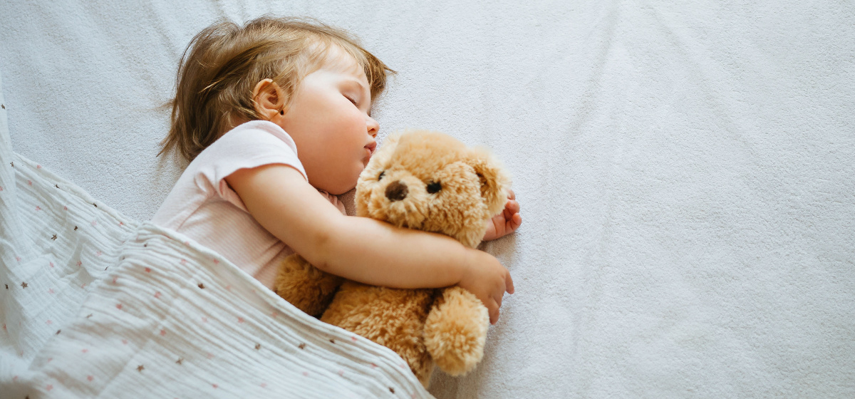 Photo d'un bébé endormi avec un ours en peluche dans un lit